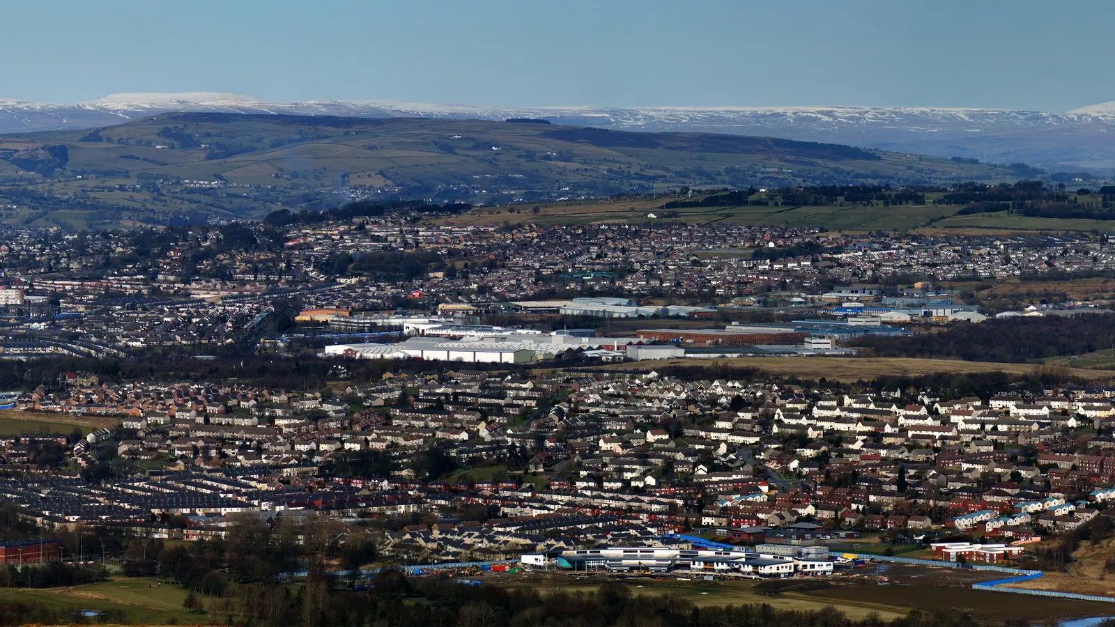 Burnley's terraced streets and industrial units across the valley, with moorland and snow-capped hills behind.