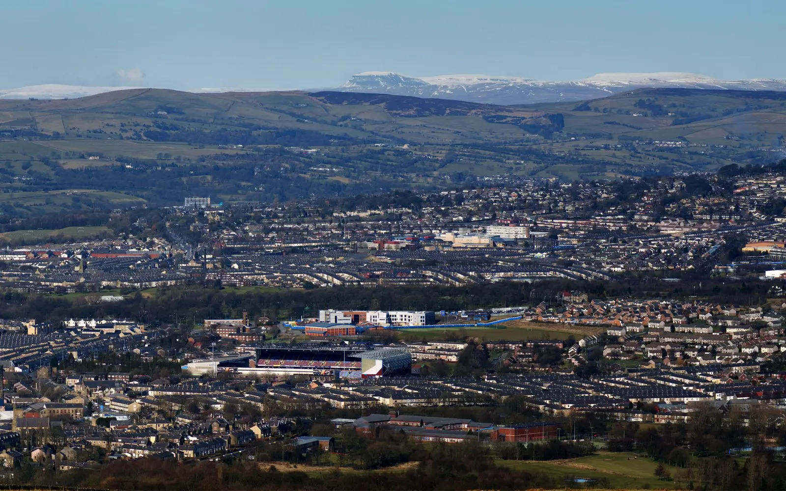 Burnley spread across the valley floor, seen from high ground, with snow on the hills beyond.