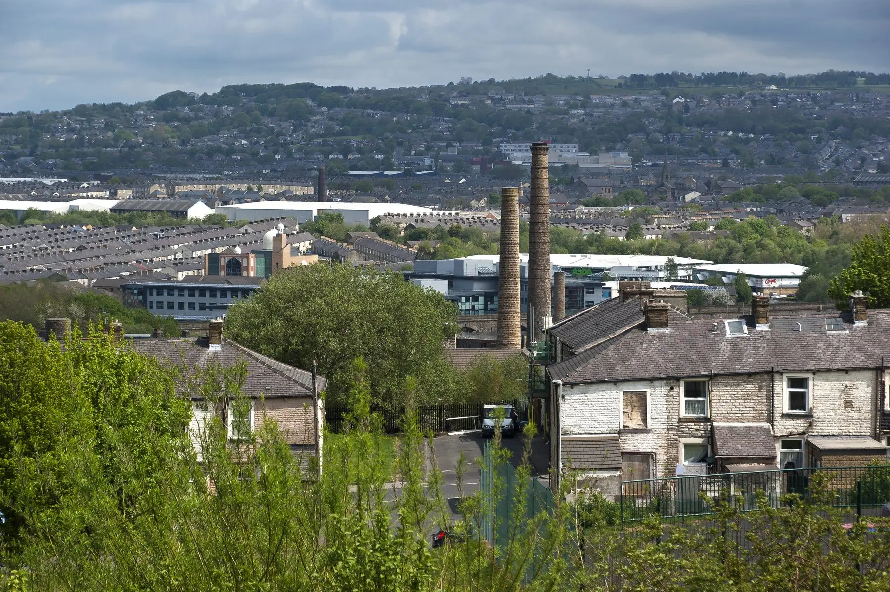 Stone terraced houses and mill chimneys in Burnley, with the town climbing the hillside behind.