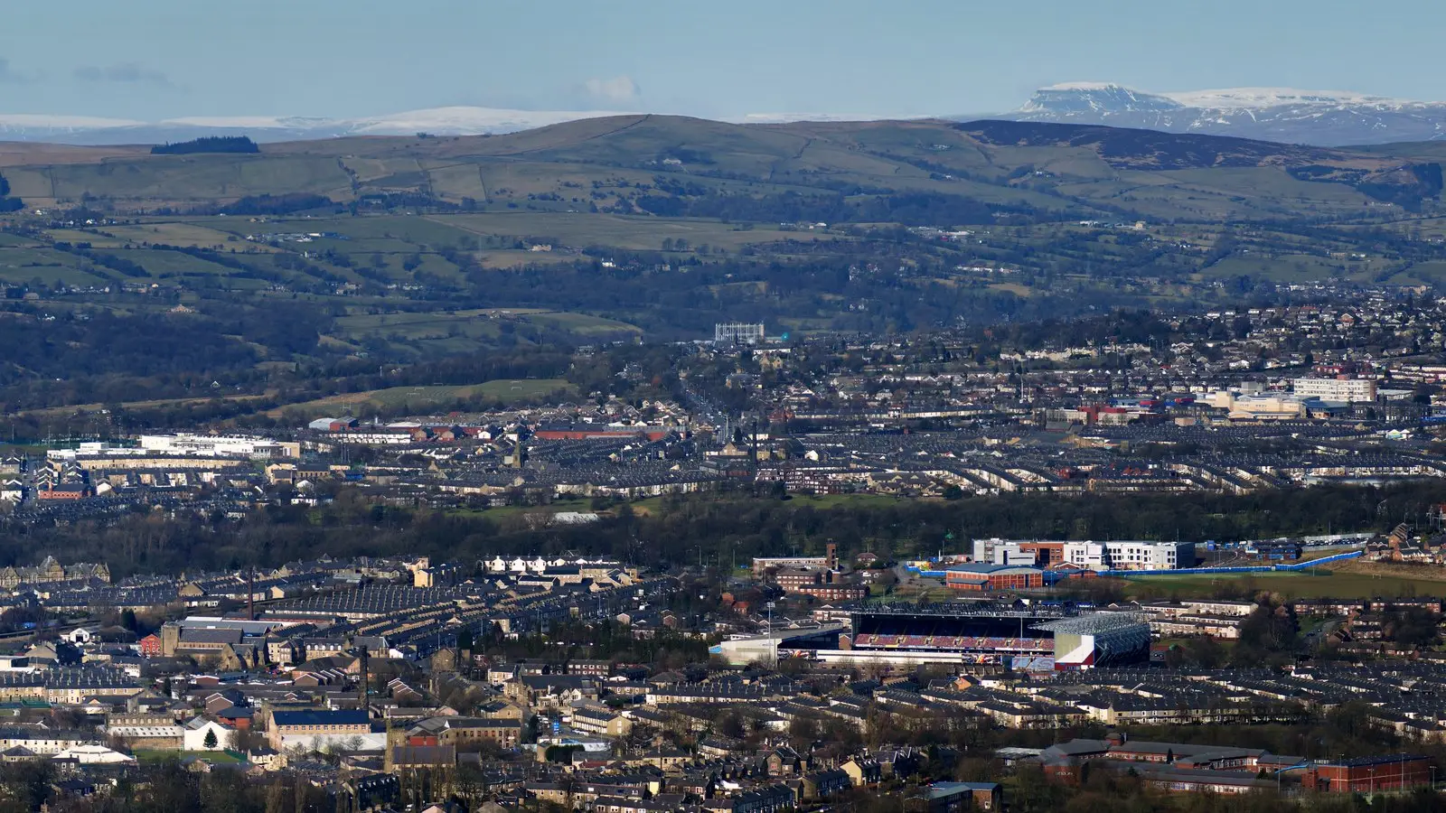 Rows of houses across Burnley, seen from above, with the hills rising behind the town.